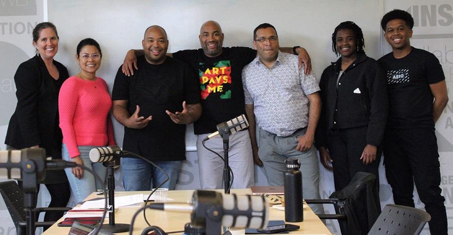 A group photo showing seven people standing near a table with microphones and other technical gear. They are a team of alumni, students and faculty who are collaborating on a number of outreach initiatives including the Loyalist Connections Podcast